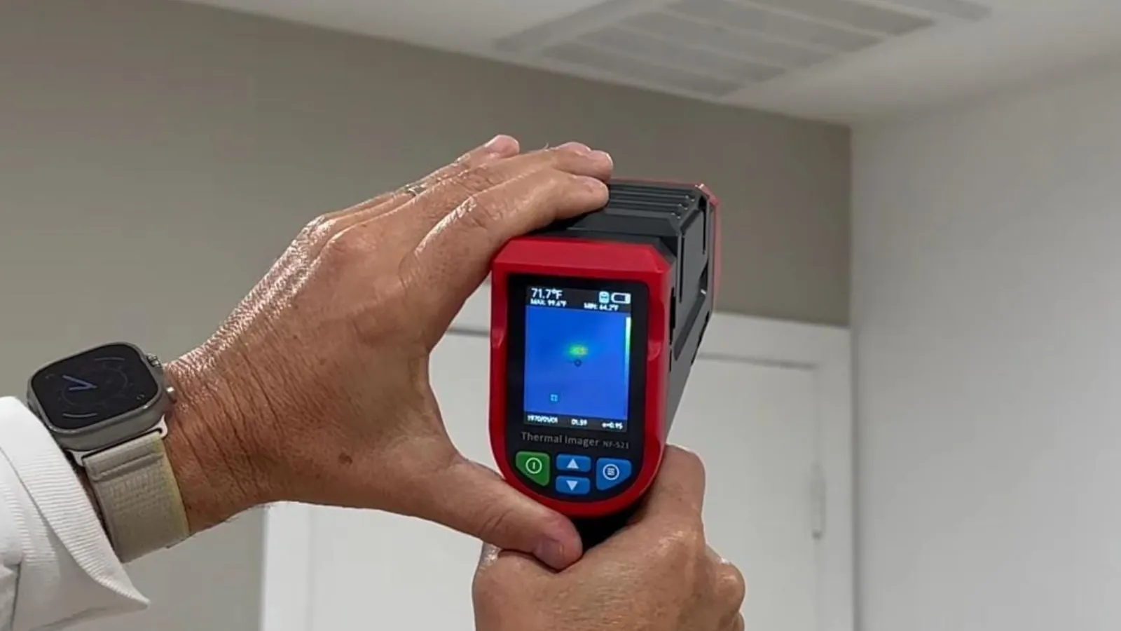 Hand holding a thermal imaging camera aimed at a wall to find a hidden leak